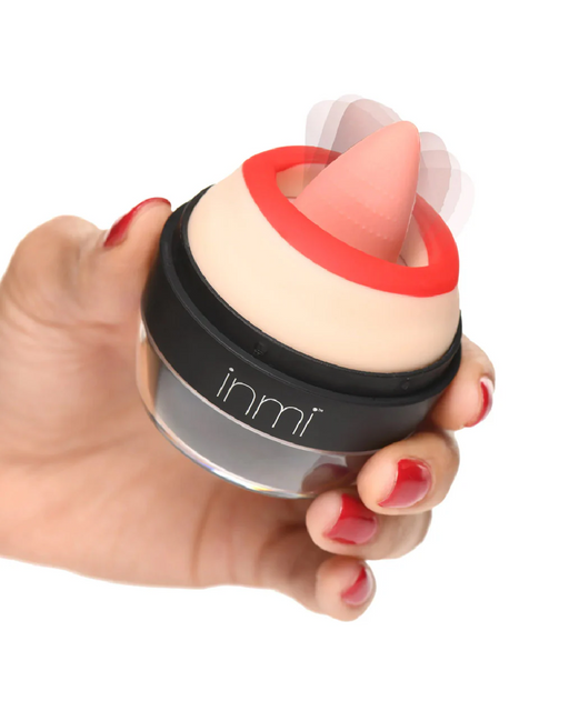 A hand with red-painted nails holds a small, round device. The device, known as the Lady Licker Rotating Tongue Stimulator with Discreet Case from XR Brands, has a black base with "inmi" written on it and a flesh-colored top. A pink, cone-shaped tip is attached to the top and there are motion lines indicating vibration, perfect for intense clitoral orgasms.