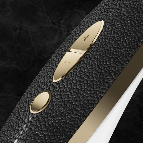 Close-up of the Satisfyer Luxury Air Pulsation + Vibration in gold and black leather set against a dark background. This sophisticated device showcases metallic volume buttons along with a round button below them. Its sleek, ergonomic handle evokes luxury and elegance, designed specifically for refined clitoral stimulation.