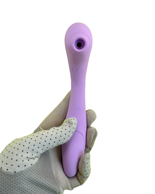 A gloved hand holds a pink handheld device with a small circular opening at one end. The Nasstoys Blaze Air Pulsation and G-Spot Bendable Double Ended Vibrator - Purple has a smooth, curved design and appears to be made of a soft material.