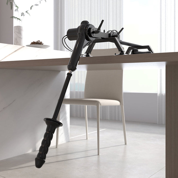 A Body Dock Thrusting Sex Machine with Remote by Pipedream Products is mounted on a tabletop in a modern, bright room with a chair in the background. The sleek device elegantly extends outward over the edge of the table.