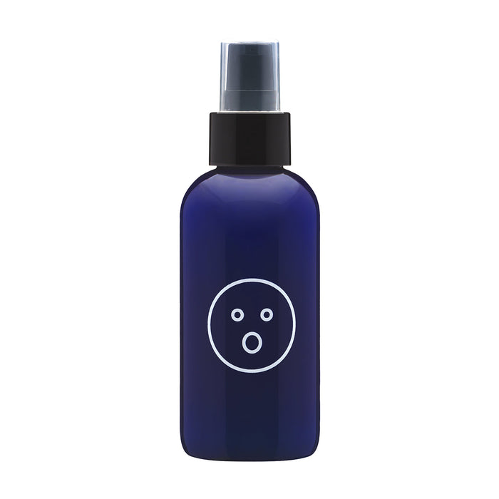 A dark blue spray bottle with a black cap and nozzle is shown against a white background. The label on the bottle features a simple white face-like design with two small circles for eyes and a larger circle for the mouth, indicating its soothing Aloe and Green Tea Extract formula. This is the Alu Aloe Vera Water Based Lubricant and Intimate Moisturizer, 4 oz by Dame Products.