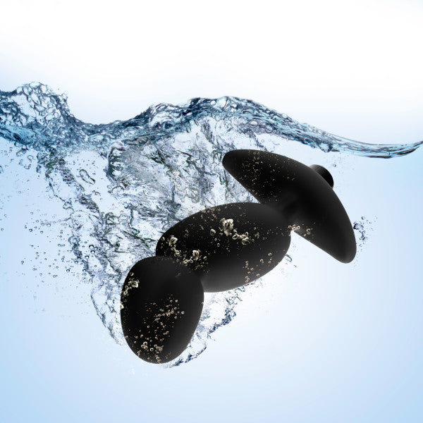 Three black stones submerged in clear water, causing splashes and bubbles, set against a gradient blue background, reminiscent of the sleek design and durable materials like those found in the Blush Anal Adventures Pinpoint Silicone Vibrating Prostate Massager.