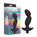 A silicone anal plug with a curved design, identified as the "Anal Adventures Pinpoint Silicone Vibrating Prostate Massager" by Blush, is shown next to its packaging. The packaging, labeled "Anal Adventures Platinum," indicates that the plug features vibrating capabilities powered by a 10-speed vibrating bullet and is made from 100% silicone. The background showcases a rainbow gradient.