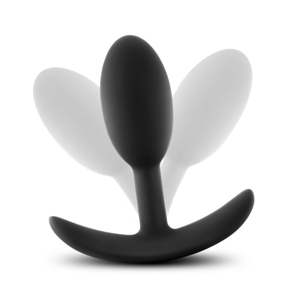 A black silicone butt plug with a flared base, known as the Anal Adventures Slim Vibra Weighted Plug - Small by Blush, is centered in the image, shown at an angle that highlights its smooth surface. Made from body-safe silicone, it's perfect for inner weight stimulation. Two translucent, white shadow-like images of the plug are in the background, creating a sense of motion and depth.