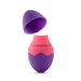 An egg-shaped device with a pink middle section labeled "Blush" and purple caps on both ends is partially uncovered at the top, revealing a wavy design where the pink and purple intersect. This Aria Flutter Tongue Clitoral Licking Oral Sex Vibrator by Blush features 7 vibration modes and appears to be made of a smooth, matte silicone material.