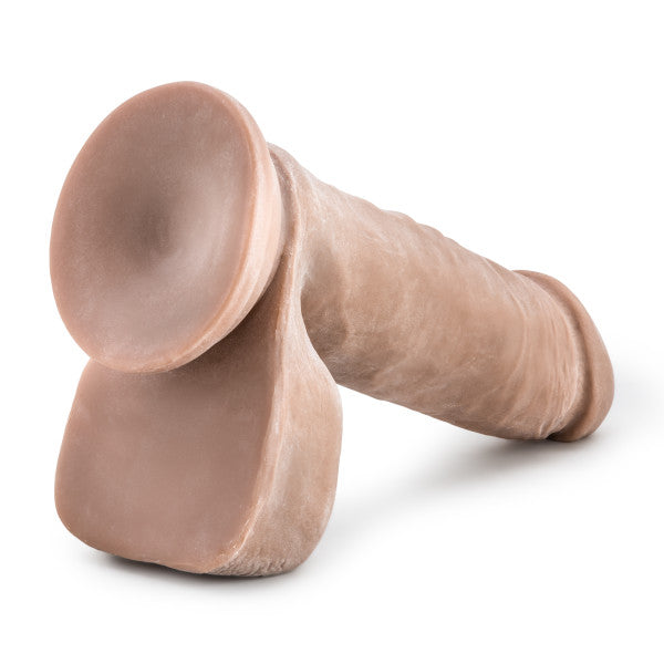 The Au Naturel 8 Inch Dual Density Suction Cup Dildo with Balls - Caramel by Blush is a realistic phallic-shaped dildo, featuring a firm texture and a suction cup base. Its 8-inch length and dual density make it perfect for strap-on play. The product is displayed lying on its side against a plain white background.