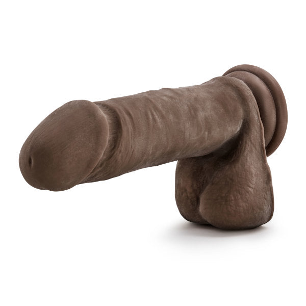 An image of the Blush Au Naturel 8 Inch Dual Density Suction Cup Dildo with Balls in Chocolate, showcasing its realistic dark brown color and detailed texture. This sex toy features a suction cup base for hands-free fun and is sculpted to resemble a penis with accompanying testicles.