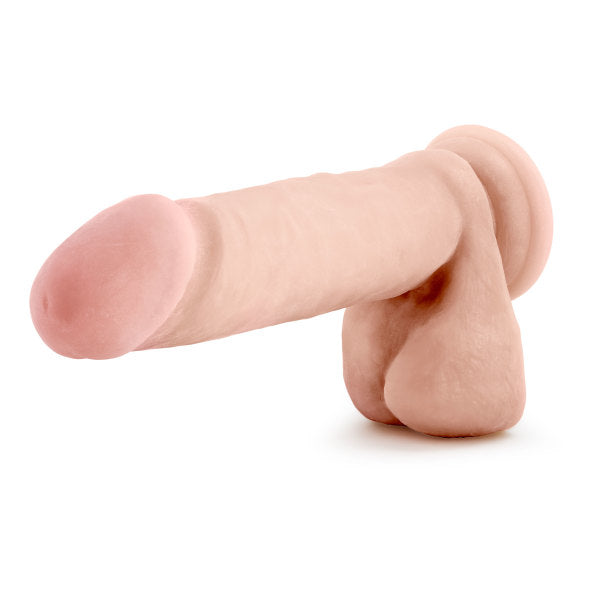 The Blush Au Naturel 8 Inch Dual Density Suction Cup Dildo with Balls in Vanilla is a realistic silicone dildo designed in a natural skin tone color. It features detailed textures including a textured shaft, a rounded tip, and a base shaped like testicles. This dildo, positioned on a plain white background, offers an authentic experience.