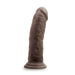 The Au Naturel 8 Inch Realistic Feel Dual Density Suction Cup Dildo - Dark Chocolate by Blush stands upright with a flared base. The lifelike veined surface texture, along with a flexible spine and strong suction cup, enhances its realism and ensures secure placement.