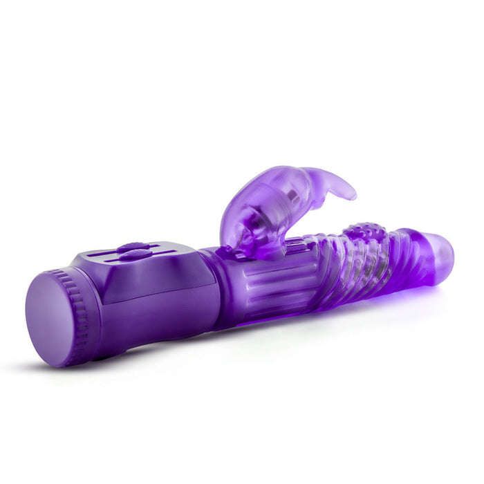 The B Yours Beginner Bunny Rabbit Vibrator by Blush is a purple, translucent device featuring a ribbed texture and a small, rabbit-shaped attachment on one end. The base includes control buttons for multiple vibrations and adjustable settings. This phthalate-free product is designed for intimate use.