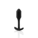 A black, silky silicone b-Vibe Snug Plug 1 Weighted Butt Plug, weighing 2 oz and featuring a smooth surface and a T-shaped base, displayed against a white background. The sleek design reflects simplicity and functionality, while its waterproof feature adds practicality.