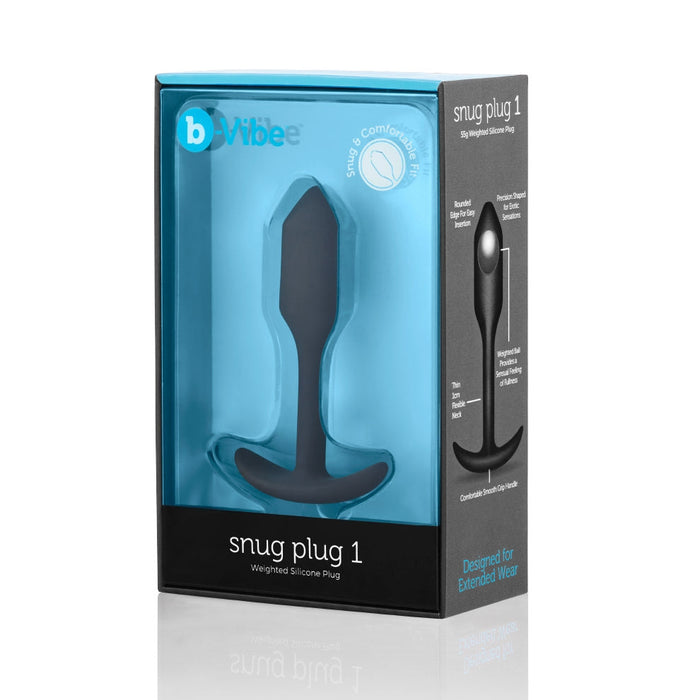 Image of a packaged product called "B-vibe Snug Plug 1 Weighted Silicone Butt Plug - 2 oz - Black" by b-Vibe. The sleek black and blue packaging showcases a black, weighted silicone plug inside a clear plastic window. The text on the package highlights features like comfort, silky silicone, waterproof design, and being designed for extended wear.