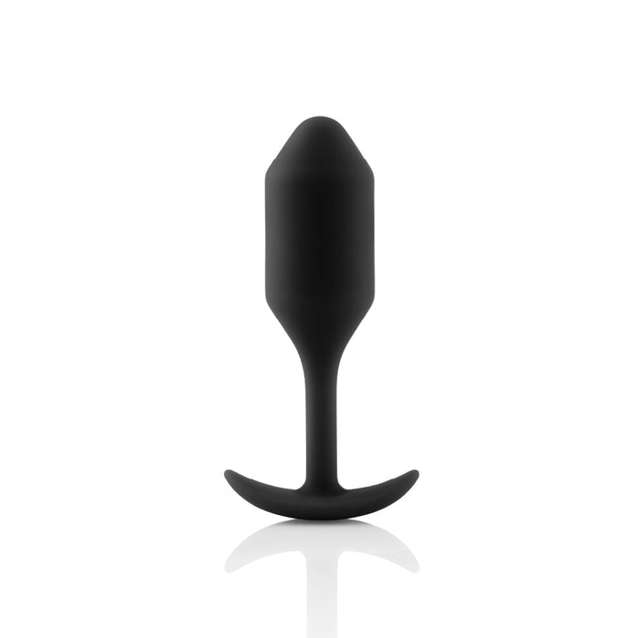 A B-vibe Snug Plug 2 Weighted Silicone Butt Plug - 5 oz - Black, featuring a smooth, rounded tip and a curved base designed for safety and comfort. This b-Vibe creation stands upright against a white background, casting a subtle reflection on the surface below it.