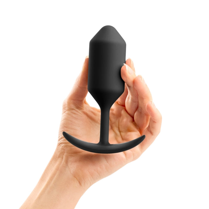 A hand holds a black B-vibe Snug Plug 3 Weighted Silicone Butt Plug, featuring a tapered tip and a curved base designed for anal play. Made from premium silicone, this waterproof anal toy stands out against the plain white background, highlighting its sleek and functional design.