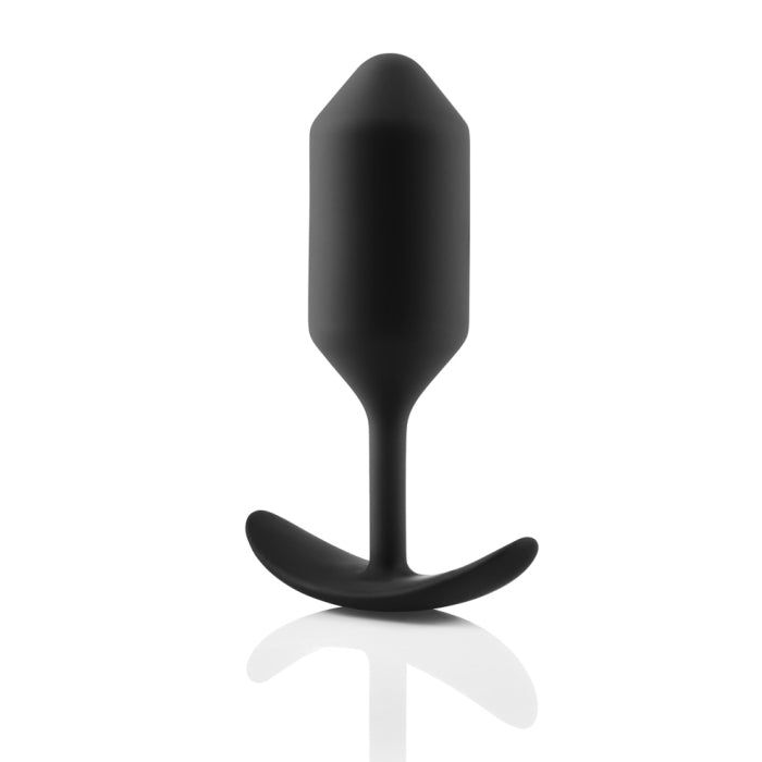 A black B-vibe Snug Plug 3 Weighted Silicone Butt Plug weighing 6 oz lies against a white background. The silicone butt plug, by b-Vibe, features a tapered tip, a slender neck, and a curved flared base with a smooth matte finish designed for comfort and safety during anal play.