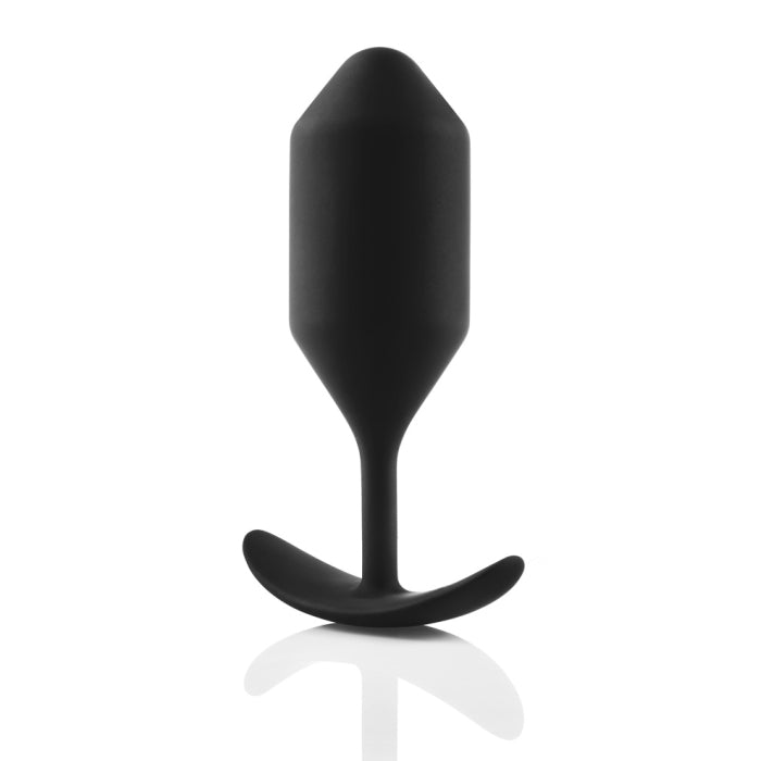 A black, cylindrical B-vibe Snug Plug 4 XL Weighted Silicone Butt Plug (9 oz) with a tapered top and a wide, curved base from b-Vibe. The reflective surface below the weighted plug creates a mirrored image. The background is solid white.