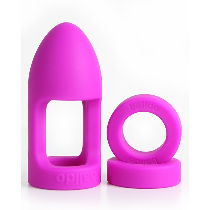 Two purple silicone items are displayed against a white background. One is a hollow, elongated, bullet-shaped item with an open center for testicle penetration, and the other is a thick, circular ring. Both items have the word "Balldo" inscribed on them and are part of Balldo: The World's First Ball Dildo collection by Balldo.