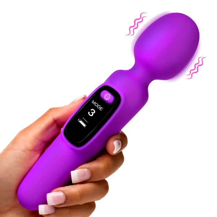 A hand holding the XR Brands' Bang! First Time Wand Vibrator with Digital Display in purple, featuring a digital screen displaying "Mode 3" and an on/off button. The wand has a bulbous head emitting illustrated vibration lines, and the hand boasts manicured nails with white polish tips.