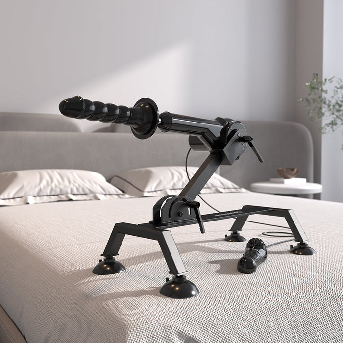 A Body Dock Thrusting Sex Machine with Remote from Pipedream Products, featuring a mechanical arm and textured attachment, is positioned on a neatly made bed in a well-lit bedroom. This sleek device is supported by a sturdy base equipped with suction cups for stability and promises robust performance. A conveniently placed remote control lies beside it for easy access.