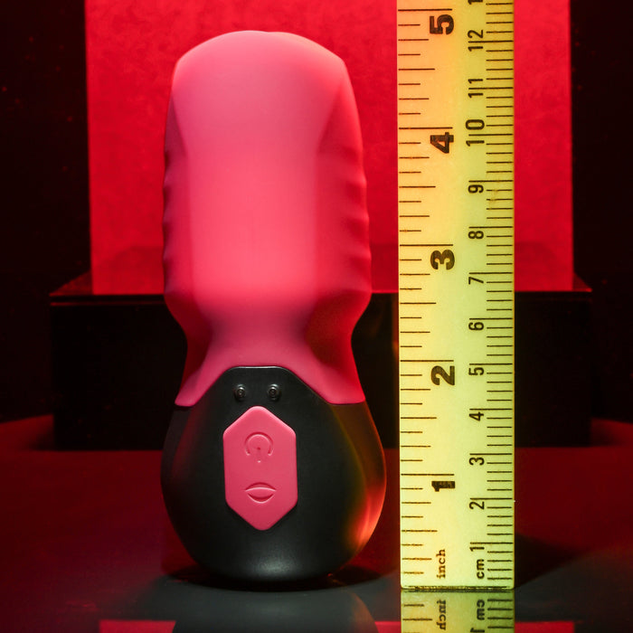 A black and red cylindrical device, possibly the Body Kisses Red Suction Masturbator and Vibrator by Evolved Novelties featuring 7 speeds, stands upright next to a yellow ruler marked in inches, measuring approximately 7.5 inches tall. The background is a gradient of black and red.