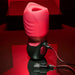 The Evolved Novelties Body Kisses Red Suction Masturbator and Vibrator, featuring a red and black design, textured grips, an opening at the top, and USB cable plugged in, is placed on a reflective red surface against a dark background. This cylindrical electronic device offers 7 speeds for customized use.