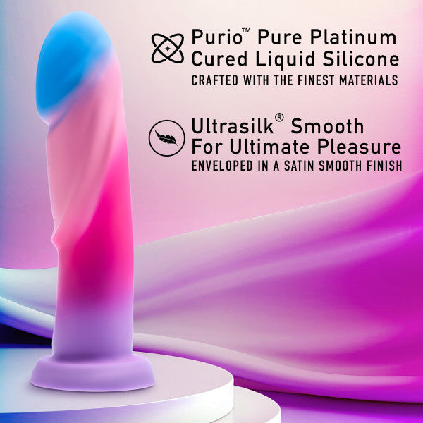 A pink and blue silicone dildo with a gradient design, labeled as the "Borealis Dreams 7.75 Inch Girthy Silicone Dildo - Cotton Candy" by Blush, sits on a white pedestal against a pink and purple gradient background. The image includes text describing the product as "Purio Pure Platinum Cured Liquid Silicone" and "Ultrasilk Smooth For Ultimate Pleasure," perfect for use with a strap-on harness.