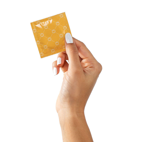 A hand with white nail polish holds a yellow wrapper from a Royal Condom Tailored Fit Vegan Condoms 20-Pack, featuring a subtle pattern and "Natural Latex Condoms" text on a crisp white background.