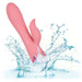 The California Dreaming Pasadena Player G-Spot Rabbit Vibrator by CalExotics is shown partially submerged in splashing water, demonstrating its waterproof feature. The pink, silicone vibrator boasts a main shaft with a textured design and a smaller, curved G-spot arm for simultaneous stimulation.