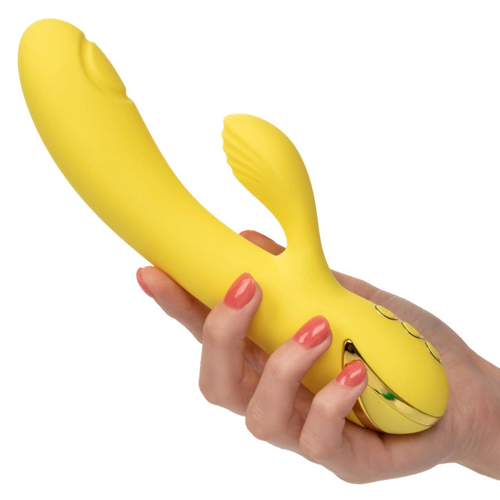 A hand with red nail polish holds the CalExotics California Dreaming San Diego Seduction G-Spot Thumping Rabbit Vibrator, a yellow, curved device featuring a small appendage for clitoral stimulation and control buttons at the base designed to enhance g-spot stimulation.