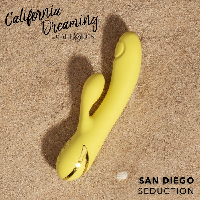 A vibrant yellow, ergonomically designed G-Spot Thumping Rabbit Vibrator is placed on sandy ground, positioned diagonally. The text reads "California Dreaming by CalExotics" in the top left corner and "San Diego Seduction" in the bottom right corner near a small seashell, promising intense sensations.