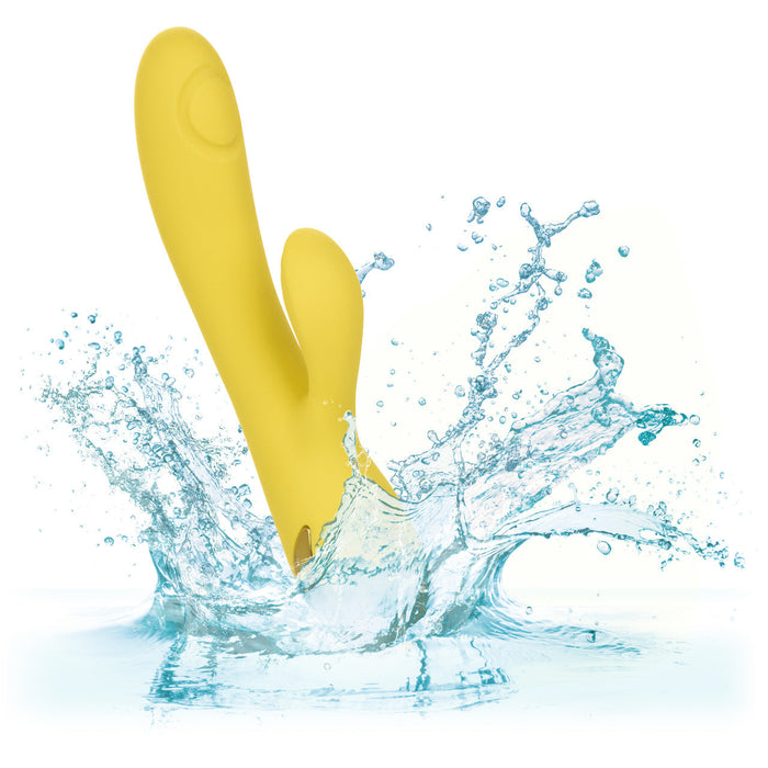 The California Dreaming San Diego Seduction G-Spot Thumping Rabbit Vibrator by CalExotics splashes into clear blue water against a white background. The yellow silicone device features a curved shape with a smaller protrusion for dual stimulation, symbolizing its waterproof capabilities and enhancing both clitoral and g-spot stimulation.