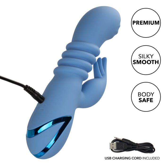 A blue, ribbed California Dreaming Santa Cruz Coaster Thrusting G-Spot Rabbit Vibrator by CalExotics with a sleek design is shown. It has a USB charging cord connected and features such as "Premium," "Silky Smooth," and "Body Safe." The waterproof Rabbit vibrator also highlights its clitoral stimulation capabilities. The image shows the separate charging cord included in the package.