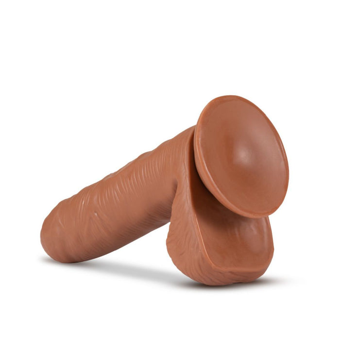 The Coverboy Derek the Bartender 7 Inch Uncut Dildo in Mocha by Blush, a brown-colored cylindrical silicone object with realistic skin texture and a ribbed design, featuring body-safe material and a suction cup base, lies on its side against a white background.