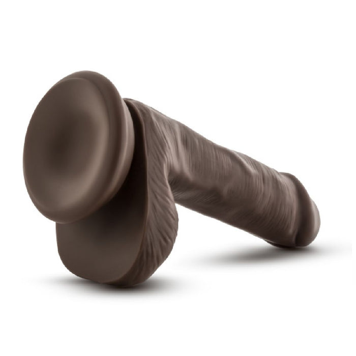 A chocolate sculpture named "Coverboy Top Gun Tommy 6 Inch Dildo - Chocolate" by Blush, shaped to resemble a realistic phallus and lying on its side. It features detailed anatomical designs with a base resembling testicles and a texture that mimics realistic skin, along with a smooth brown surface typical of chocolate.