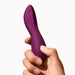 A hand holds the Dame Dip Beginner's Internal & External Silicone Vibrator - Plum, a curved and smooth premium silicone product from Dame Products, designed for personal use and commonly recognized as a sex toy. The object boasts a sleek and ergonomic design suitable for intimate stimulation. It features multi-pattern vibration settings and is fully waterproof. The background is plain and white.