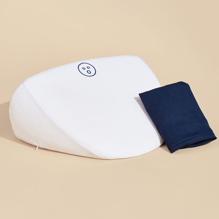 A white, wedge-shaped Dame Pillo Sex Pillow for Sex Positioning - Indigo with a small circular logo in the center from Dame Products is positioned against a beige background. A folded navy blue fabric cover is placed next to the pillow.