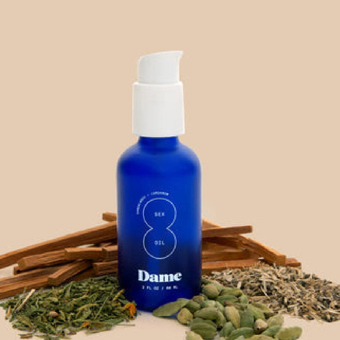 Dame Sex Oil for Intimate Massage blue bottle with ingredients surrounding bottle on beige background 