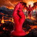 A large XR Brands Demon Claw Fisting Silicone Dildo, crafted from high-quality silicone, stands upright amidst a fiery landscape with molten lava and rocky terrain. In the background, a muscular winged demon with horns and claws stands on a rock. The sky is filled with dark, ominous clouds and blazing fire.