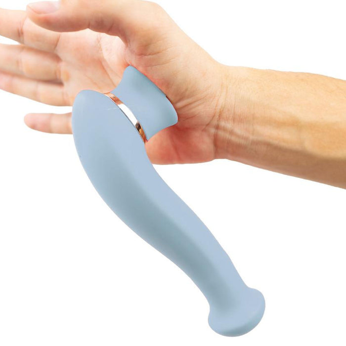 A person's hand is holding the Destiny Blue Clitoral Suction Vibrator with Tongue by Maia Toys. This sleek clitoral sucking toy features a smooth surface, a rounded tip, and a silver ring near the base. Made from body-safe silicone materials, it ensures enhanced safety. The background is plain white.