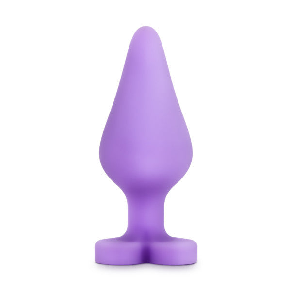 The Do Me Now Naughty Candy Heart Purple Butt Plug by Blush is a teardrop-shaped, hypoallergenic, phthalate-free silicone butt plug that stands upright, featuring a smooth surface and a flared base.