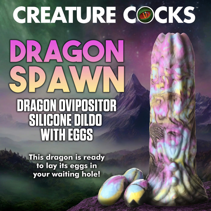 Promotional image showcasing a fantastical silicone dildo, designed to mimic the vibrant tail of a dragon. The text reads, "XR BRANDS DRAGON SPAWN DRAGON OVIPOSITOR SILICONE FANTASY ROLE PLAY DILDO WITH EGGS. This dragon is primed to lay its eggs in your eagerly awaiting hole!" The background features a mystical landscape with majestic mountains and a luminous sky.