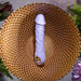 The Purple Fantasy Veiny Silicone Vibrator with Finger Loop, in a soothing lavender hue, sits on a textured gold-toned plate. Graced by green foliage and purple flowers, the setting exudes an inviting and serene vibe.