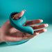 A hand holds the Thumbs Up Shallow Penetration Vibrator with Finger Loop, a teal silicone sex toy with a smooth, curved design. The finger loop ensures ease of use. The matching teal background enhances the product's color.