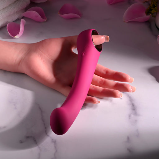 A hand holds the pink Pleasure Curve G-Spot Vibrator with Finger Loop, resting on marble. Soft, scattered rose petals create an intimate setting for exploring its waterproof vibrations.