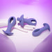 The Hole Punch Vibrating 3 Piece Anal Training Set, featuring purple silicone plugs with handle-like loops for enhanced anal sensations, is displayed on a white mannequin hand against a purple gradient backdrop that creates a soft and warm ambiance.