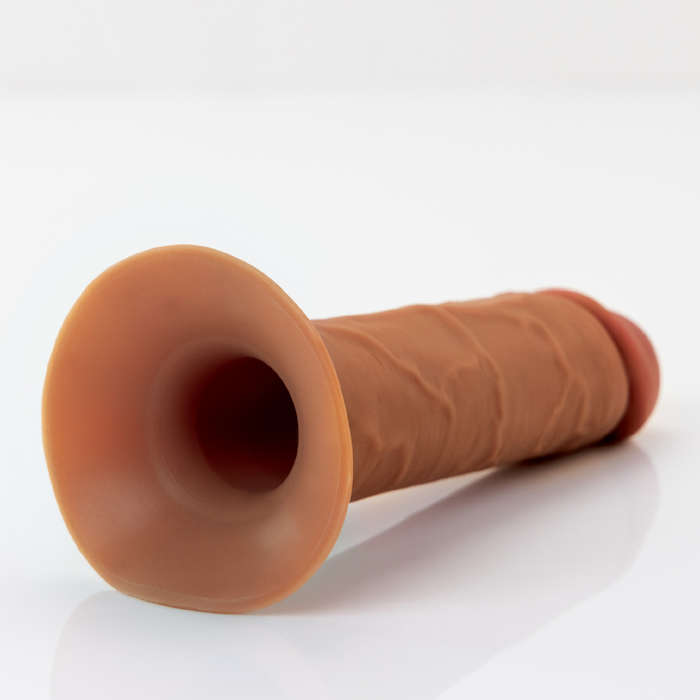 The Fantasy X-Tensions Elite Hollow 6 Inch Silicone Dildo & Strap-On Harness - Chocolate by Pipedream Products, crafted from dual-density silicone and featuring a suction cup base, is placed horizontally on a plain, white surface. This dildo boasts a textured surface designed to resemble human anatomy.