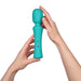 Two hands holding the FemmeFunn Ultra Wand Silicone Vibrator in blue, featuring a turquoise-textured finish, a rounded head, and a hexagonal pattern. The waterproof massager boasts small embossed icons, including a lightning bolt and the initials "FF," on the front of the handle. The background is white.