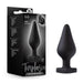 A black Fuck Me Silicone Heart Butt Plug from Blush, featuring a tapered shape and heart-shaped base, is displayed alongside its predominantly black packaging, which includes an image of the product and text that reads "Temptasia Fuck Me Plug.”