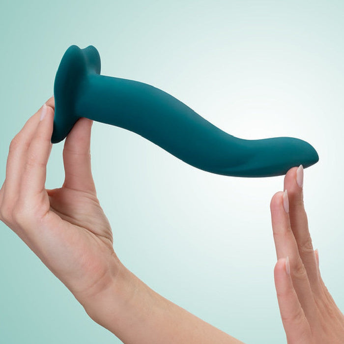 A person holding a Fun Factory Limba Flex Medium Silicone Dildo in Deep Sea Blue against a light blue background. The dildo, designed with a smooth finish and an ergonomic shape, features a suction base.