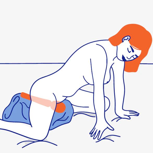 A minimalistic illustration depicts a woman with orange hair, on her hands and knees, leaning forward. Beside her rests the Fun Factory Vim Silicone Weighted Rumbly Wand Vibrator - Orange, its silicone handle visible. A blue cushion is placed under her pelvis, while an orange strip provides support across her hips. The scene is set against a plain background.